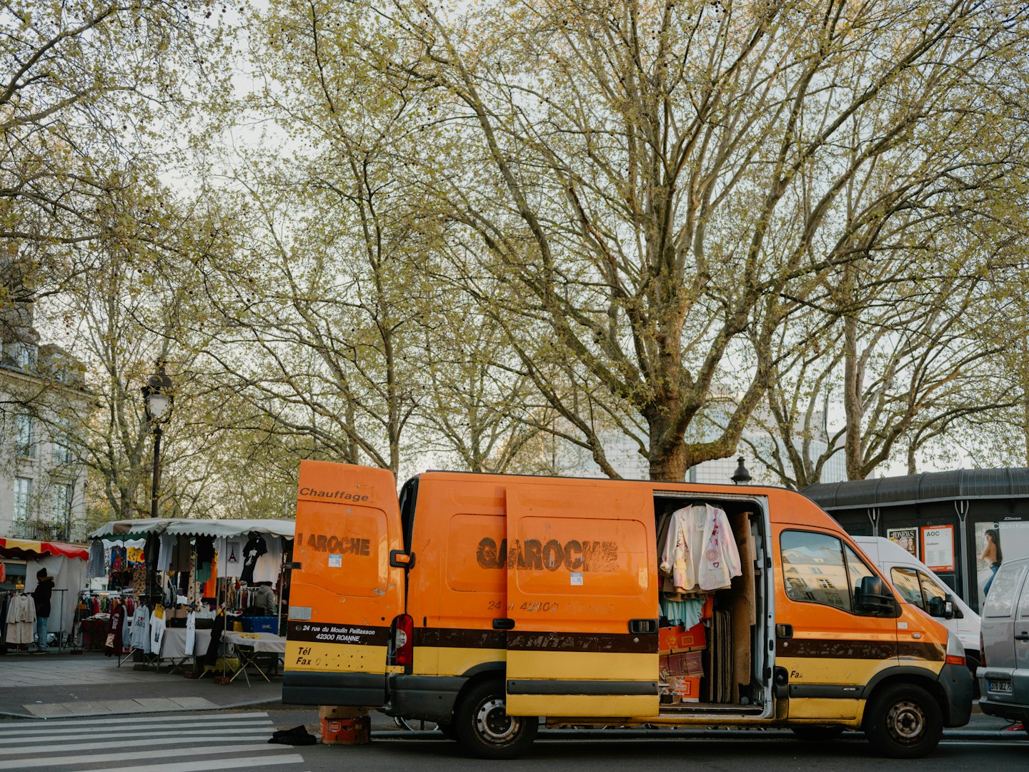 Oranssi ja keltainen huoltoauto avoimilla ovilla kaupungin kadulla.